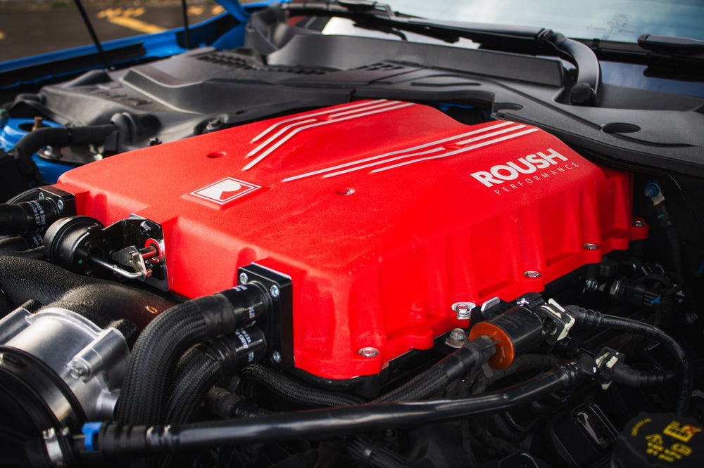 
                  
                    Close-up of a red Roush Performance engine cover inside a car. The engine, boasting 740 horsepower with its Supercharger Kit, is highlighted by attached cables and tubes.
                  
                