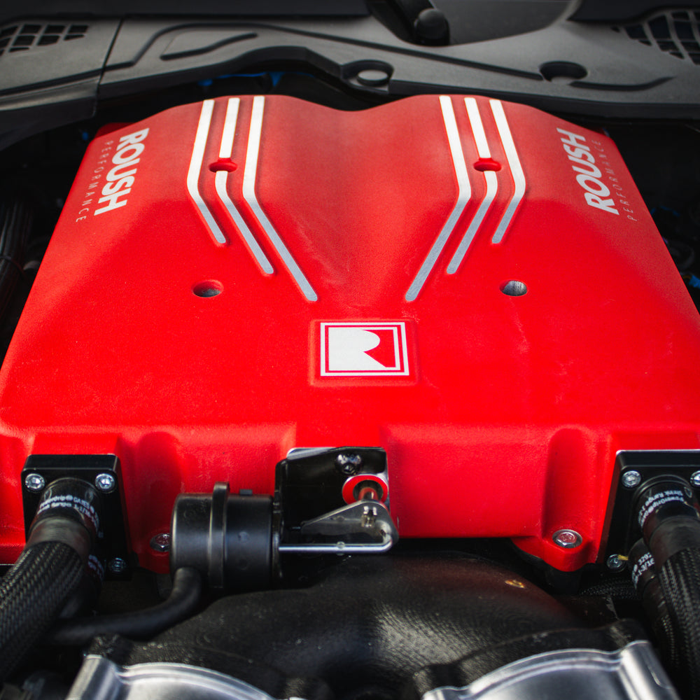 
                  
                    Close-up view of a Roush Performance engine cover in red with silver stripes and logo, highlighting the power of the 740-horsepower Roush S650 Mustang.
                  
                