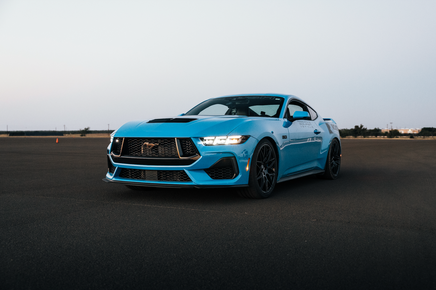 
                  
                    A blue sports car, equipped with aggressive drop and Roush Mustang Lowering Springs, is parked on a wide, empty asphalt surface under a clear sky.
                  
                